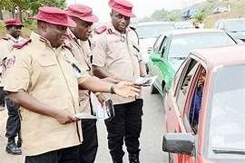 Traffic officers wearing uniforms and hats talking to a driver in a red car on a busy road.