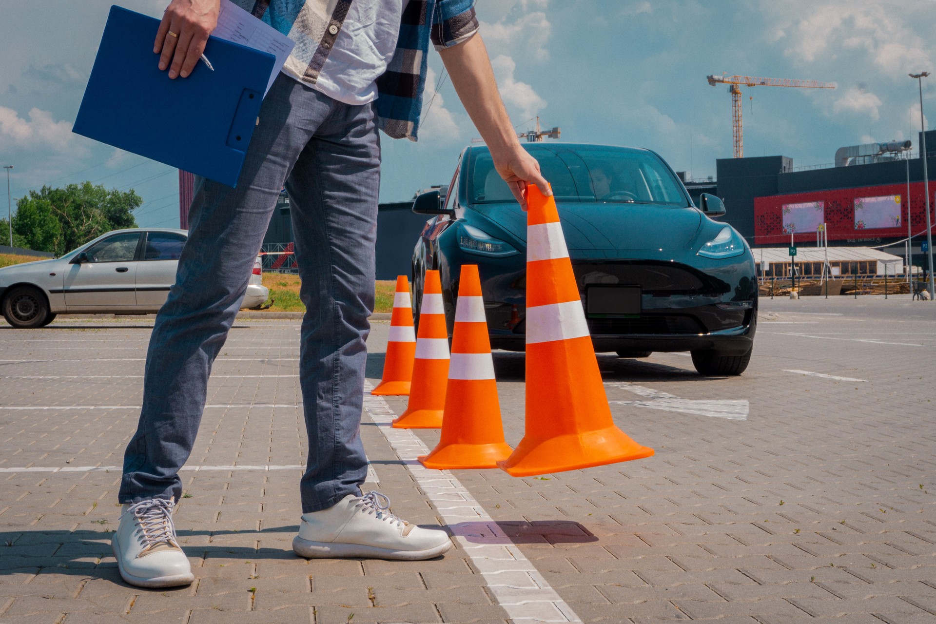 Instructor near car with his female student during exam at driving school test track. Man putting the traffic cones. Driving test, driver courses, exam concept